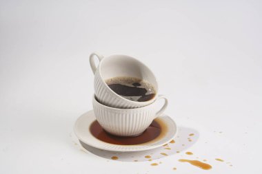 Beyaz bir yüzey üzerinde beyaz bir tabak üzerinde başka bir kupaya istiflenmiş kapuçino dolu beyaz bir porselen bardak.