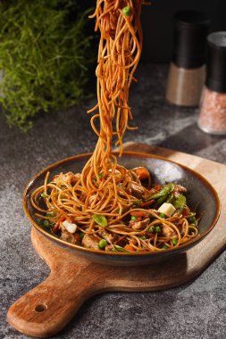 İtalyan spagettisi, tavuk, yeşil fasulye, peynirli mozzarella ve yeşil kase içinde gri beton yüzeyde tahta üzerinde taze kekik ile çatal tutan kadın eli.