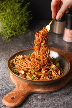 İtalyan spagettisi, tavuk, yeşil fasulye, peynirli mozzarella ve yeşil kase içinde gri beton yüzeyde tahta üzerinde taze kekik ile çatal tutan kadın eli.