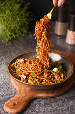 İtalyan spagettisi, tavuk, yeşil fasulye, peynirli mozzarella ve yeşil kase içinde gri beton yüzeyde tahta üzerinde taze kekik ile çatal tutan kadın eli.