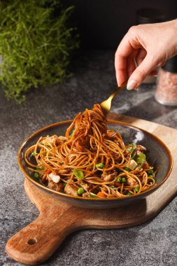 İtalyan spagettisi, tavuk, yeşil fasulye, peynirli mozzarella ve yeşil kase içinde gri beton yüzeyde tahta üzerinde taze kekik ile çatal tutan kadın eli.