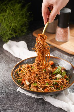 İtalyan spagettisi, tavuk, yeşil fasulye, peynirli mozzarella ve yeşil kase içinde gri beton yüzeyde tahta üzerinde taze kekik ile çatal tutan kadın eli.
