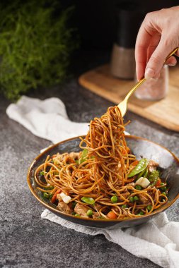 İtalyan spagettisi, tavuk, yeşil fasulye, peynirli mozzarella ve yeşil kase içinde gri beton yüzeyde tahta üzerinde taze kekik ile çatal tutan kadın eli.