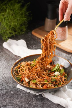 İtalyan spagettisi, tavuk, yeşil fasulye, peynirli mozzarella ve yeşil kase içinde gri beton yüzeyde tahta üzerinde taze kekik ile çatal tutan kadın eli.