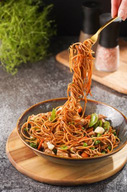 İtalyan spagettisi, tavuk, yeşil fasulye, peynirli mozzarella ve yeşil kase içinde gri beton yüzeyde tahta üzerinde taze kekik ile çatal tutan kadın eli.