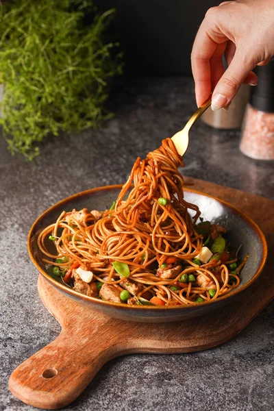 İtalyan spagettisi, tavuk, yeşil fasulye, peynirli mozzarella ve yeşil kase içinde gri beton yüzeyde tahta üzerinde taze kekik ile çatal tutan kadın eli.