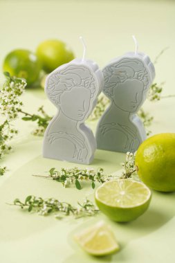 Limonlar ve ağaç dallarıyla çevrili, nane yeşili arka planda Yunan tanrıçası şeklinde iki gri ve mavi mum.