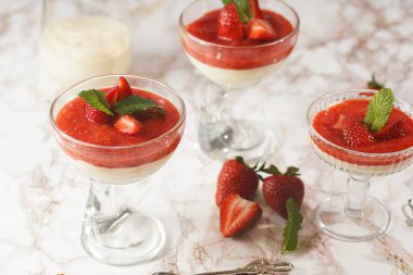 Geleneksel kremalı tatlı panna cotta ile birkaç bardak naneli ve çilekli reçelli mermer yüzeyde taze çilek