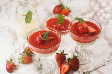 Geleneksel kremalı tatlı panna cotta ile birkaç bardak naneli ve çilekli reçelli mermer yüzeyde taze çilek