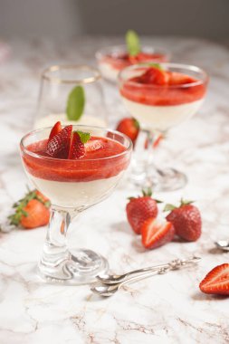 Geleneksel kremalı tatlı panna cotta ile birkaç bardak naneli ve çilekli reçelli mermer yüzeyde taze çilek
