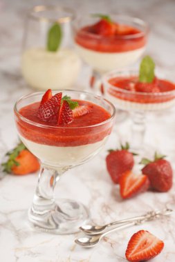 Geleneksel kremalı tatlı panna cotta ile birkaç bardak naneli ve çilekli reçelli mermer yüzeyde taze çilek