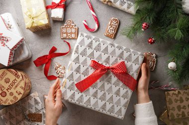 Beyaz şekerli zencefilli kurabiyeler. Gri bir yüzeyde ev şeklinde. Noel süslemeleri ve hediye tutan kadın elleri.