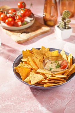 Peynirli tortilla cipsi ve pembe mermer yüzeyinde acılı peynir sosu, vişneli domates, sabah ışığında ketçap.