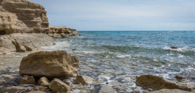 Kıbrıs 'taki Zapalo Sahili' nin kayalık bir kıyı şeridi ve yumuşak deniz dalgalarıyla manzarası, Akdeniz sahillerinin barışçıl ve doğal güzelliklerini yansıtıyor.