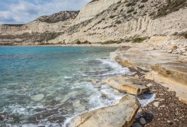 Kıbrıs 'taki Zapalo Sahili' nin kayalık bir kıyı şeridi ve yumuşak deniz dalgalarıyla manzarası, Akdeniz sahillerinin barışçıl ve doğal güzelliklerini yansıtıyor.