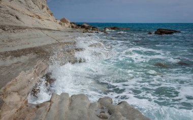 Kıbrıs Rum Kesimi 'ndeki kayalık Zapalo Sahili' nin manzarası. Deniz dalgaları sahile vuruyor, sıçramalar ve ferahlatıcı bir kıyı atmosferi yaratıyor.