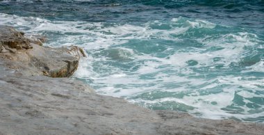 Kıbrıs Rum Kesimi 'ndeki kayalık Zapalo Sahili' nin manzarası. Deniz dalgaları sahile vuruyor, sıçramalar ve ferahlatıcı bir kıyı atmosferi yaratıyor.