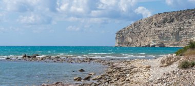  Kıbrıs 'taki Zapalo Körfezi' nin turkuaz deniz, açık bulutlar, kayalık uçurumlar ve açık hava altında kumlu bir sahili manzarası