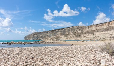  Kıbrıs 'taki Zapalo Körfezi' nin turkuaz deniz, açık bulutlar, kayalık uçurumlar ve açık hava altında kumlu bir sahili manzarası