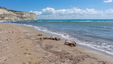 Kıbrıs 'taki Zapalo Körfezi' nin turkuaz deniz, açık bulutlar, kayalık uçurumlar ve açık hava altında kumlu bir sahili manzarası