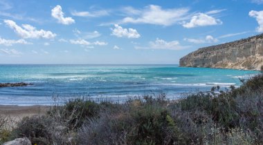 Kıbrıs 'taki Zapalo Körfezi' nin turkuaz deniz, açık bulutlar, kayalık uçurumlar ve açık hava altında kumlu bir sahili manzarası