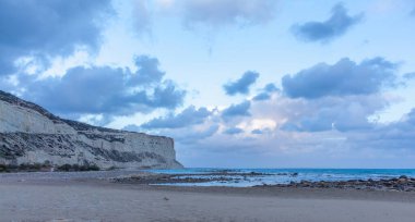 Akşamları huzurlu Kıbrıs plajı kayalık kayalıklar, yumuşak sahil şeridi ve alacakaranlıkta sakin bir kum.