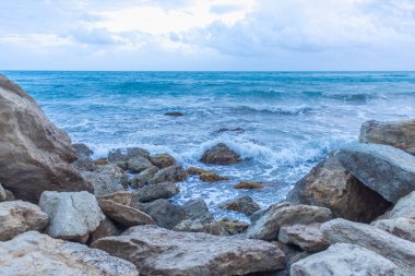 Alacakaranlıkta sakin Kıbrıs plajı, ön planda kayalar, sakin deniz ve huzurlu bir sahil havası yaratan serin mavi akşam tonları.