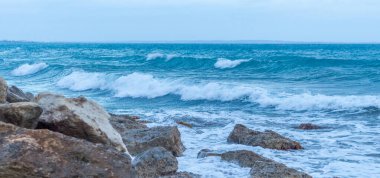Alacakaranlıkta sakin Kıbrıs plajı, ön planda kayalar, sakin deniz ve huzurlu bir sahil havası yaratan serin mavi akşam tonları.
