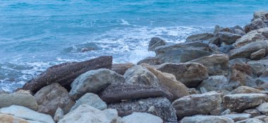 Alacakaranlıkta sakin Kıbrıs plajı, ön planda kayalar, sakin deniz ve huzurlu bir sahil havası yaratan serin mavi akşam tonları.