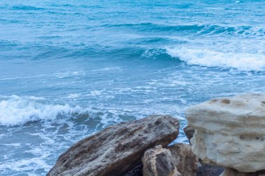 Alacakaranlıkta sakin Kıbrıs plajı, ön planda kayalar, sakin deniz ve huzurlu bir sahil havası yaratan serin mavi akşam tonları.
