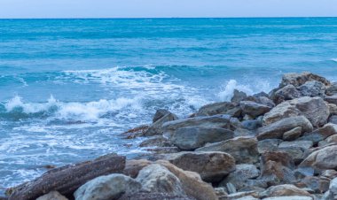 Alacakaranlıkta sakin Kıbrıs plajı, ön planda kayalar, sakin deniz ve huzurlu bir sahil havası yaratan serin mavi akşam tonları.