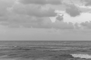 Uzak bir ufuk ile sakin deniz ve dağınık bulutlar siyah beyaz Kıbrıs 'ın sakin sahil atmosferini yakalıyor.