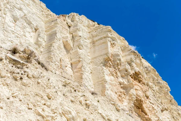  Kıbrıs sahilindeki beyaz kayalıkların alçak açılı manzarası seyrek bitki örtüsü ve parlak mavi gökyüzü doğal kıyı güzelliğini gözler önüne seriyor.