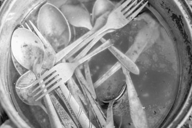 Kirli kaşık ve çatallarla dolu bir tencerenin tek renkli fotoğrafı suya batırılmış, dokuları, yansımaları ve günlük mutfak hayatını renklendiriyor.