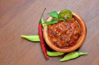 Baharatlı fesleğen yaprakları ve limon dilimleriyle süslü ahşap bir kasede acı biber ezmesi (sambal terasi). seçici odak