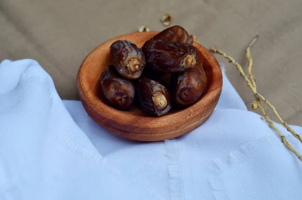 Tarihler (Phoenix dactylifera) beyaz ve kahverengi kumaş arka planda bir ahşap kase üzerinde. Müslümanlar için Ramazan ayında oruç tutmak. seçici odak