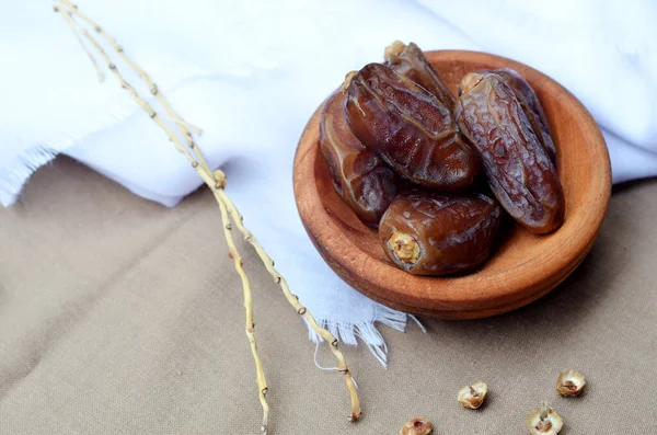 Dates (Phoenix dactylifera) on a wooden bowl on a white and brown cloth background. food for breaking the fast during Ramadan for Muslims. selective focus