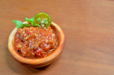 Baharatlı fesleğen yaprakları ve limon dilimleriyle süslü ahşap bir kasede acı biber ezmesi (sambal terasi). seçici odak