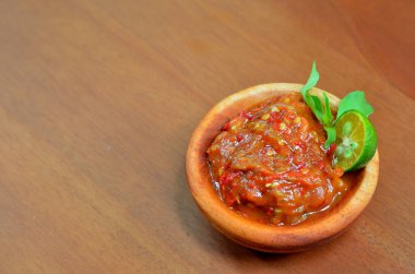 Baharatlı fesleğen yaprakları ve limon dilimleriyle süslü ahşap bir kasede acı biber ezmesi (sambal terasi). seçici odak
