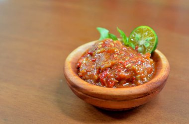 Baharatlı fesleğen yaprakları ve limon dilimleriyle süslü ahşap bir kasede acı biber ezmesi (sambal terasi). seçici odak
