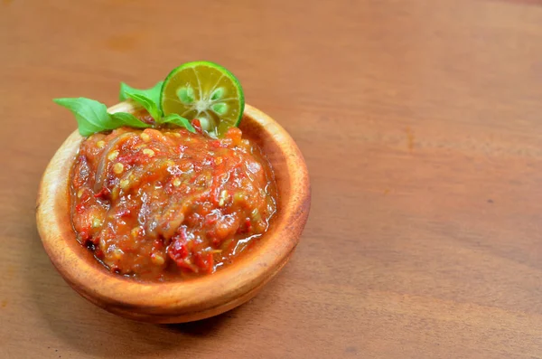 Baharatlı fesleğen yaprakları ve limon dilimleriyle süslü ahşap bir kasede acı biber ezmesi (sambal terasi). seçici odak