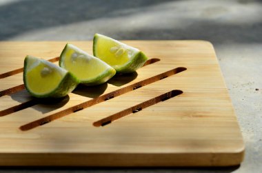 Tahta bir tepside üç limon (Citrus aurantiifolia). Genellikle sıcak havası olan tropikal restoranlarda kullanılır. Seçici odaklı sol üst görünüm