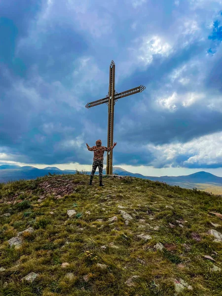 A man prays on a mountain in front of a cross-beautiful wallpaper, clouds and nature