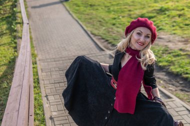 Güzel bir kız merdivenlerden yukarı çıkıyor, hem bordo palet hem de biet giymiş, siyah dudaklı bir yetişkin, sonbaharda mavi bulutların arkasında..