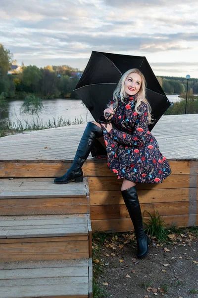 Dívka s tmavým deštníkem sedí na dřevěném schodišti na pozadí oblohy na jevišti. s charismatickým vzhledem — Stock fotografie