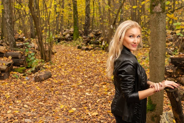 Nel bosco, una ragazza indossa una giacca di pelle e jeans neri. guardando concetto di benessere della fotocamera — Foto Stock