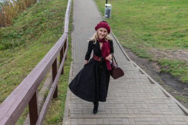 Güzel bir kadın merdivenlerden yukarı çıkar ve bordo pist ve biet ile, siyah elbiseli güzel bir gülümsemesi olan bir yetişkin, sonbaharda bir gölün arka planında, mavi bulutların üzerinde yürür..