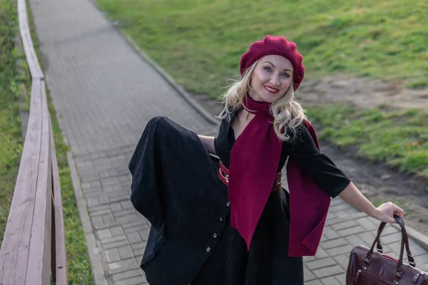 Bir kız merdivenlerden yukarı çıkar ve bordo palet ve biet ile, siyah elbiseli bir yetişkin kameraya gülümser, sonbaharda mavi bulutların arka planına karşı..