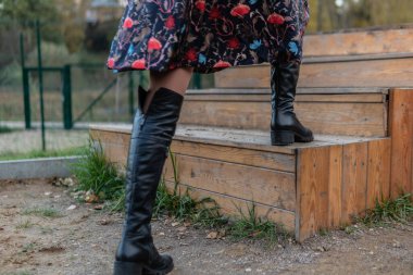 Bir bayan merdivenlerden yukarı çıkar ve bordo pall ve biret, siyah giysiler içinde, sonbaharda göletin arka planında mavi gökyüzü.