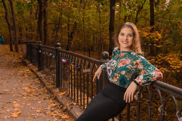 Uma menina sorri de pé em uma ponte no outono na floresta — Fotografia de Stock